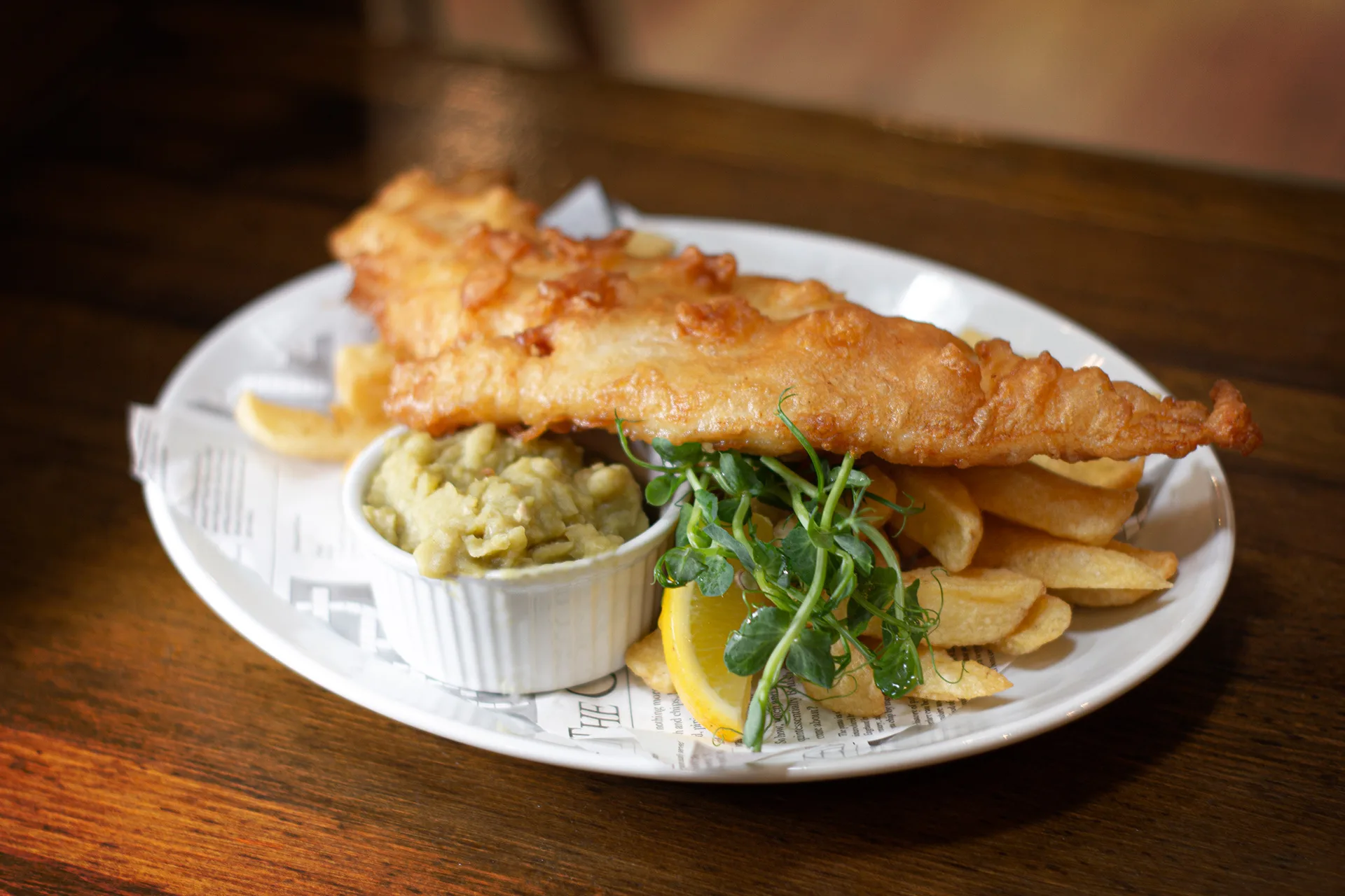 A white plate that has battered fish and chips on it.