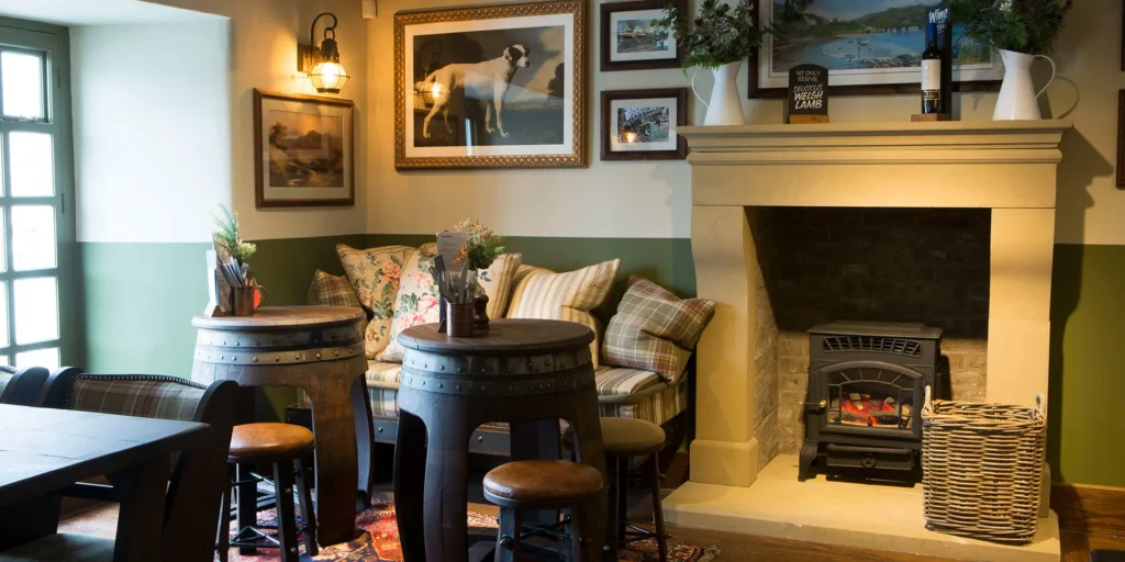 Decor in a pub. There is some pictures on the wall, a green couch with several pillows on there. There is also a wooden table with seats around it
