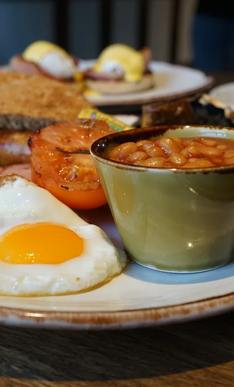 A white plate that has beans, fried egg and tomato on it