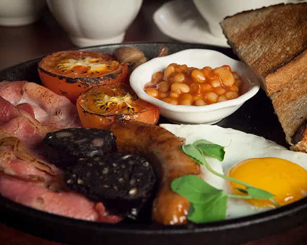 A black plate with bean, fried egg, sausage, bacon and tomato on it