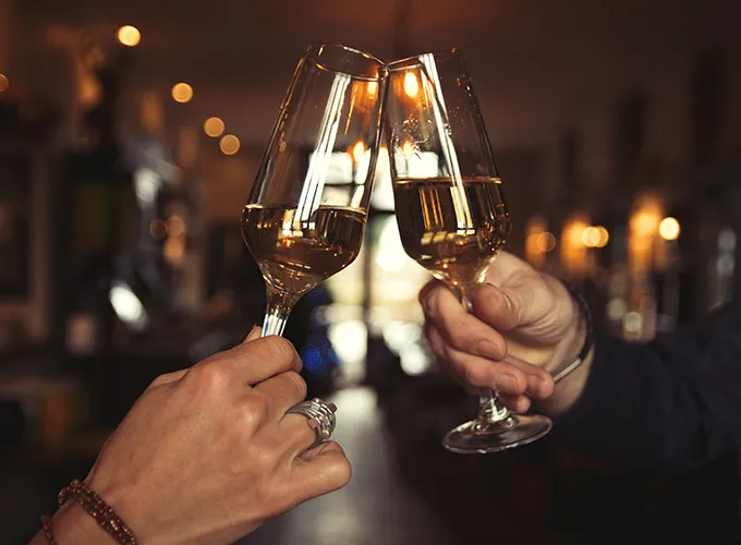 Two people holding wine glasses and clinking them