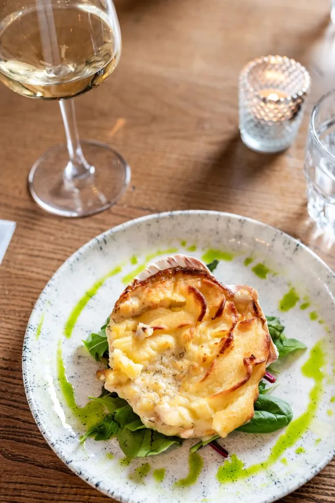 A white plate with coquille on it, Underneath the coquille is green sauce.