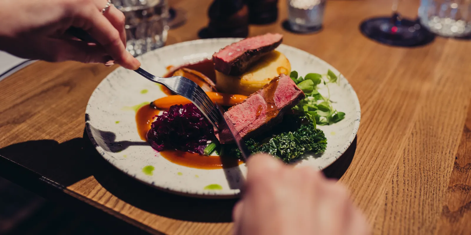Someone cutting into duck breast on a plate. The duck breast is on top of gravy and vegetables.