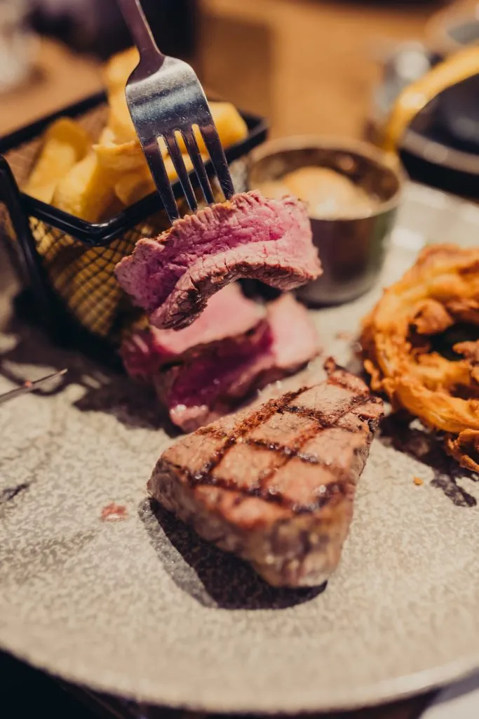 Someone cutting into beef on a plate. Next to the beef is steak and chips.