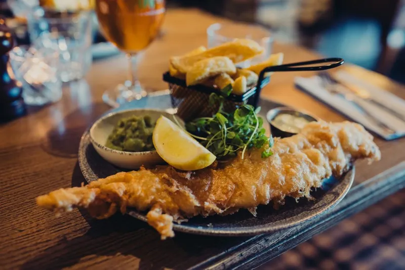 A grey plate with battered fish, lemon, salad, chips and peas