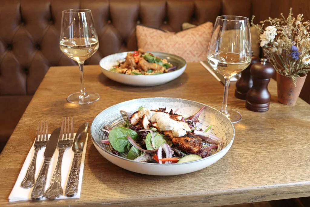 Two plates of food on the table. Next to one of the plates is cutlery and wine glasses.