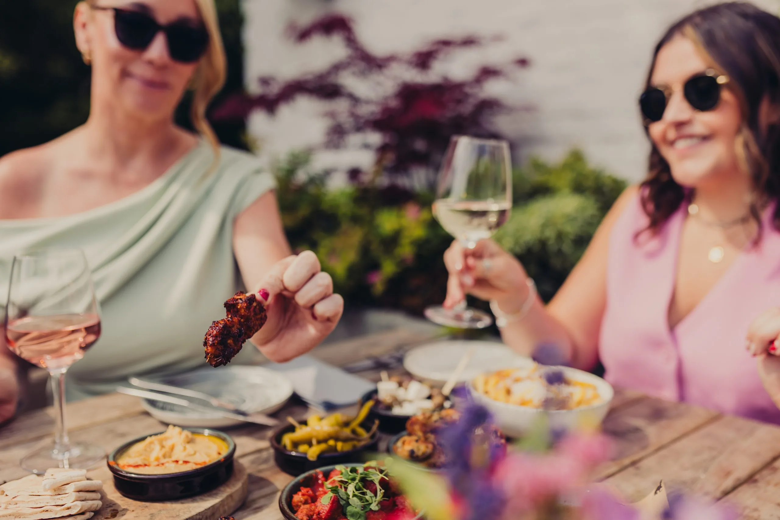 Two ladies sitting at the table. The table has various dishes on it. They're holding glasses on wine.