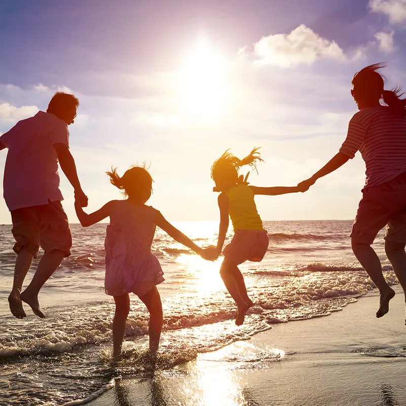 A family jumping on the beach, next to water